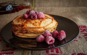 A photo of pancakes with raspberries on top, being covered in maple syrup.