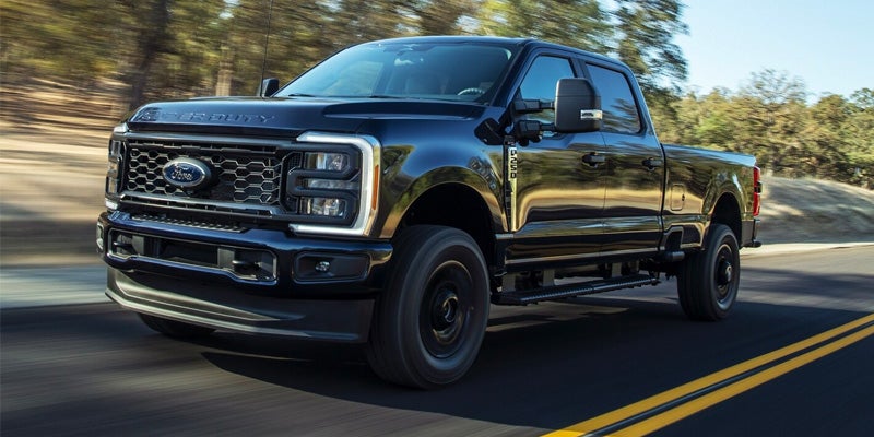 A black 2024 Ford F-250 driving down the highway on a sunny day